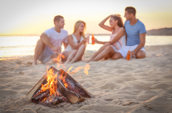 two couples having drinks on the beach in front of a fire
